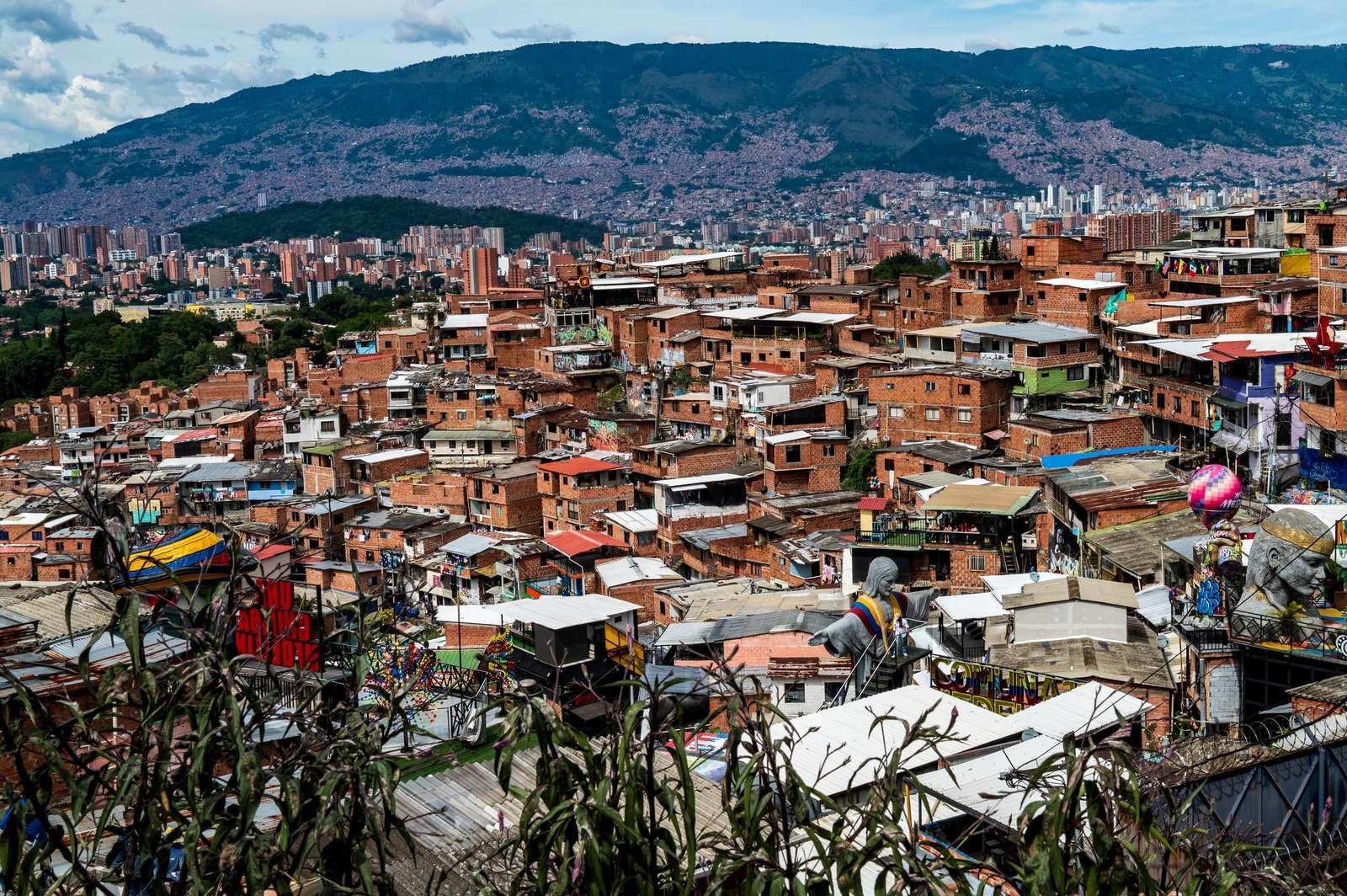 Panorama Comuny 13 z pomnikiem Chrystusa na dachu budynku, w tle góry i centrum Medellín.