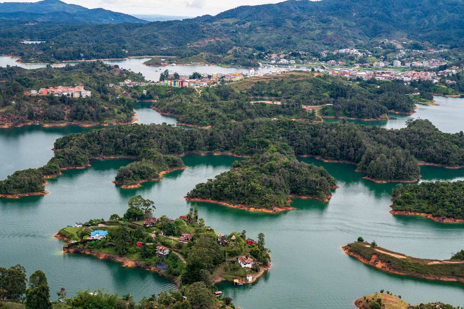 Widok z lotu ptaka na zalew Guatape, wyspy porośnięte lasem i miasteczko w tle.
