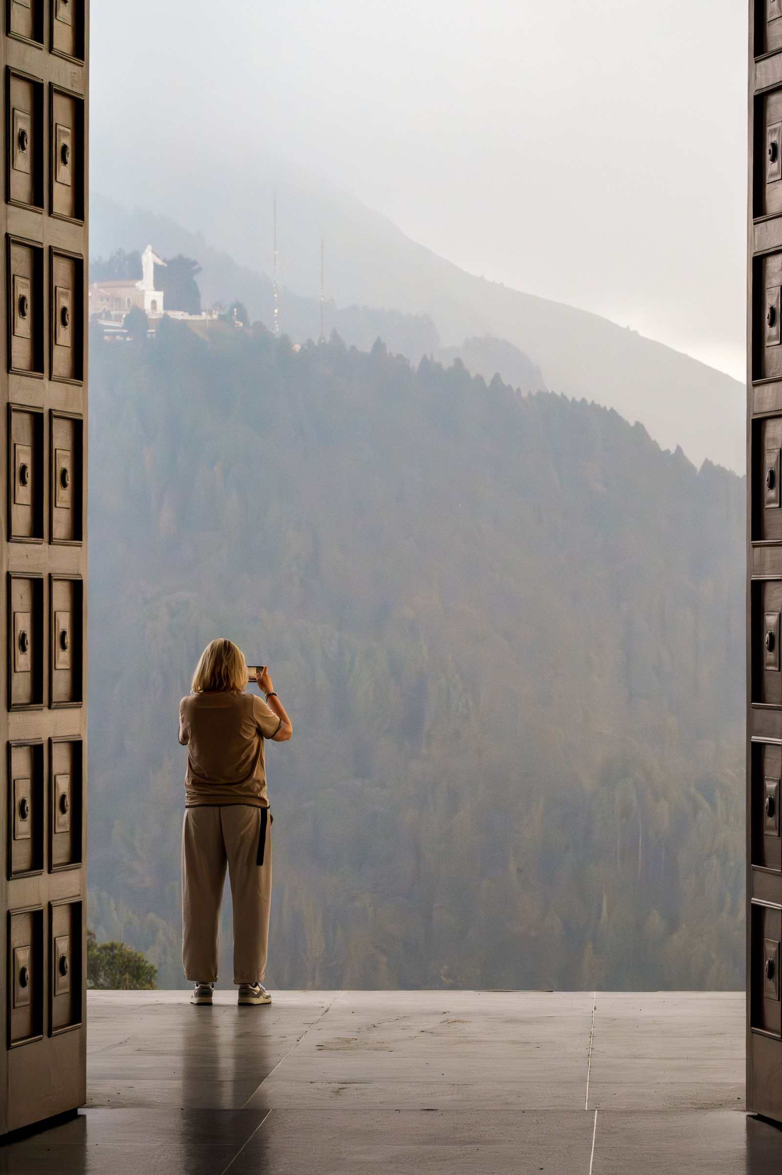 Kobieta fotografująca telefonem pomnik Cristo Rey z tarasu na Monserrate w Bogocie, we mgle.