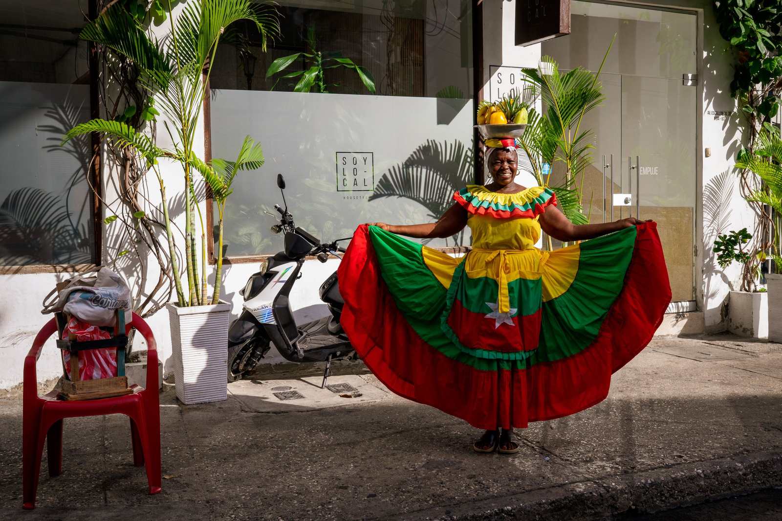 Palenquera tańcząca w kolorowej sukni z miską owoców na głowie.